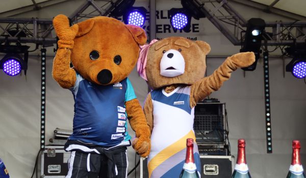 Zwei Bären-Maskottchen winken auf einer Bühne.