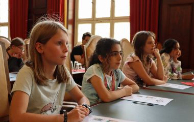 Kinder sitzen an Tischen nebeneinander.