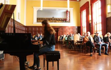 Eine Frau sitzt an einem Flügel und spielt. Im Hintergrund sitzt das Publikum im Rathaussaal.