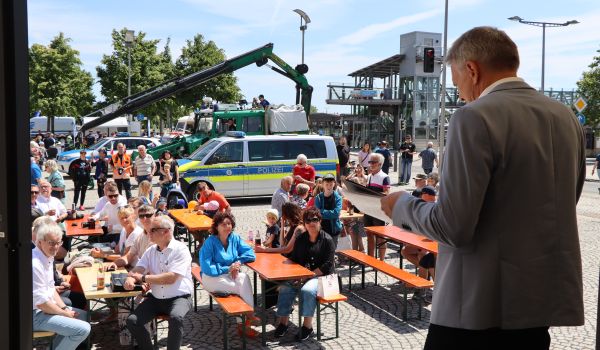 Der Bürgermeister begrüßt Menschen, die vor einer Bühne auf dem Rathausplatz sitzen.