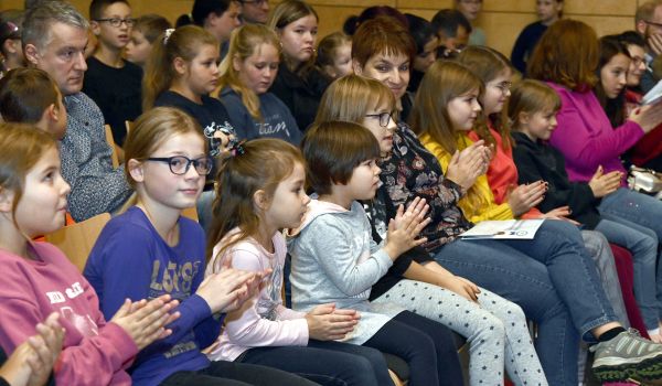 Kinder und Erwachsene sitzen in Stuhlreihen und klatschen.