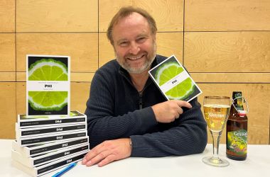 Ein Mann sitzt an einem Tisch und hält ein Buch in der Hand.