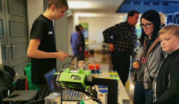 Jugendliche an einem Stand mit 3-D-Druckteilen.