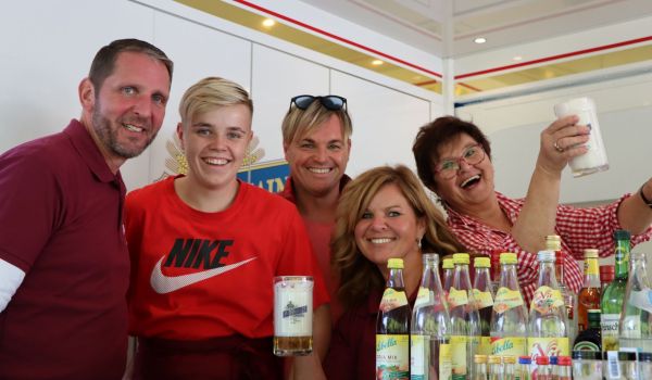 Fünf Personen stehen in einem Verkaufsauto. Vor ihnen stehen verschiedene Flaschen auf einem Tisch.