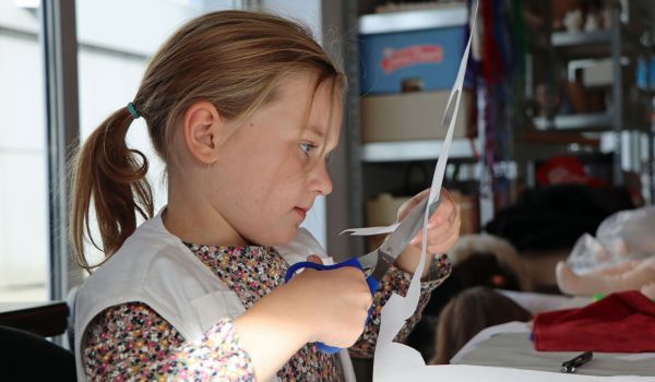 Ein kleines Mädchen schneidet mit einer Schere ein Stück Papier aus.