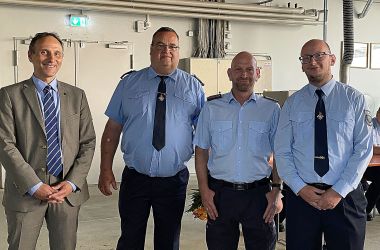 Drei Feuerwehrmänner in Uniform stehen nebeneinander. Links davon steht ein Mann im Anzug. Es ist der Hauptamtliche Beigeordnete Christian Dressel.