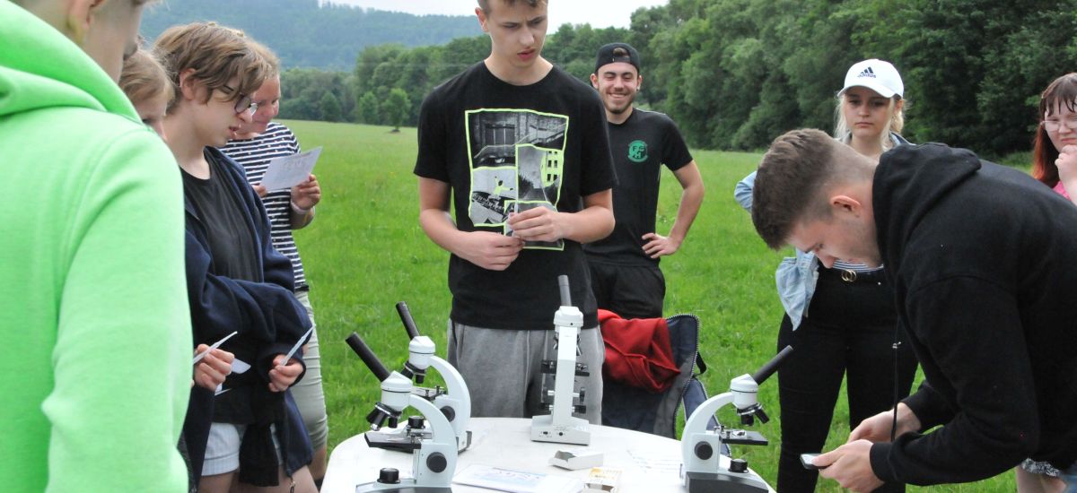 Jugendliche stehen um einen Tisch herum. Auf dem Tisch stehe Mikroskope.