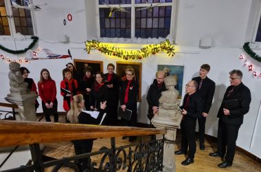 Ein Chor mit Männern und Frauen steht auf einem Treppenabsatz und singt.