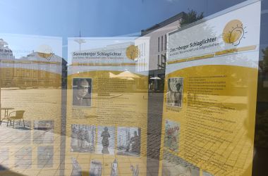 Drei Info-Banner stehen hinter einer Glasscheibe.