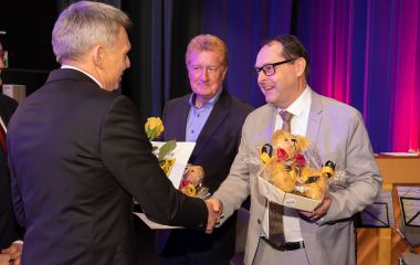 Der Bürgermeister überreicht Präsente an zwei Männer.