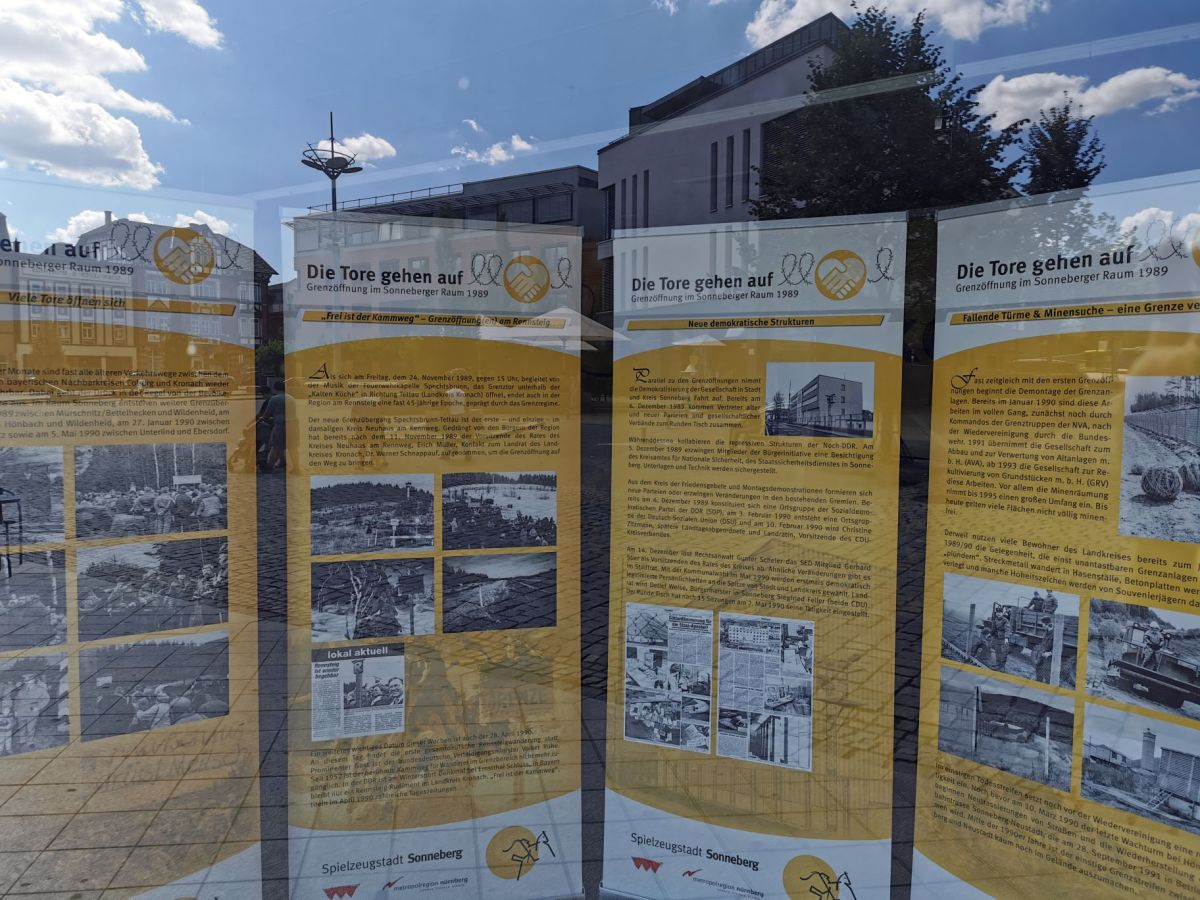 Vier Banner stehen hinter einer Glasscheibe. Die Banner tragen die Überschift: Die Tore gehen auf - Grenzöffnung im Sonneberger Raum. Es sind alte Bilder und informative Texte darauf zu sehen.
