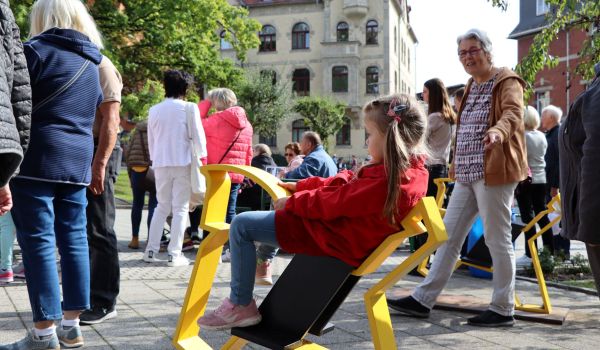 Ein kleines Mädchen sitzt auf einer gelben Pferdekonstuktion aus Metall. Es ist das Pferd des Sonneberger Reiterleins. Im Hintergrund stehen viele Menschen.