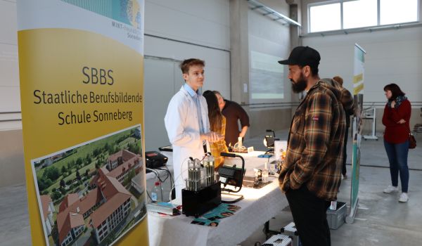 Menschen stehen an einem Messestand und unterhalten sich.