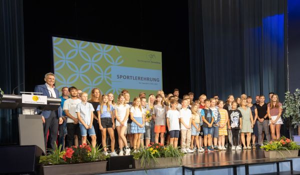 Viele Kinder und Erwachsene stehen auf einer Bühne.