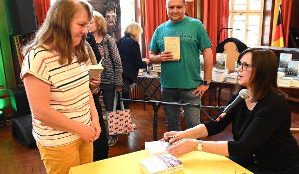 Eine Frau signiert Bücher in einem Saal.