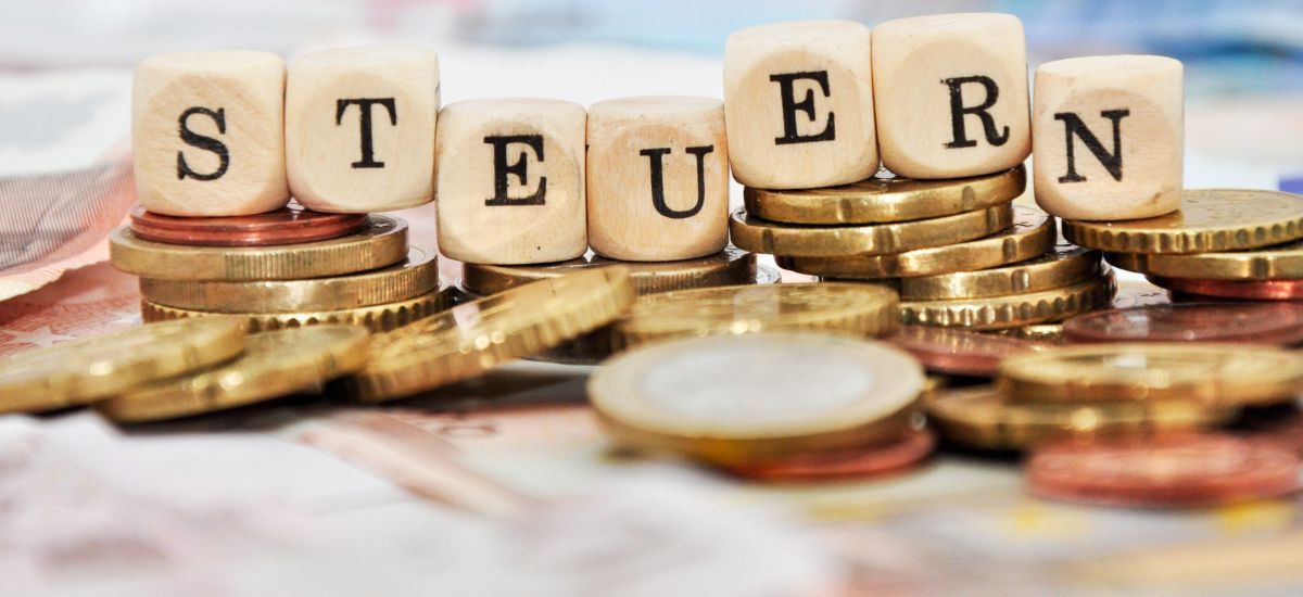 Das Wort Steuern steht auf Würfeln. Darunter liegt Geld.