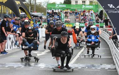 Menschen werden auf Bürostühlen über eine Rennstrecke geschoben.