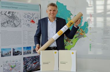 Ein Mann im Anzug hält eine Rolle mit Bauunterlagen in den Händen. Es ist der Bürgermeister der Stadt Sonneberg Dr. Heiko Voigt.