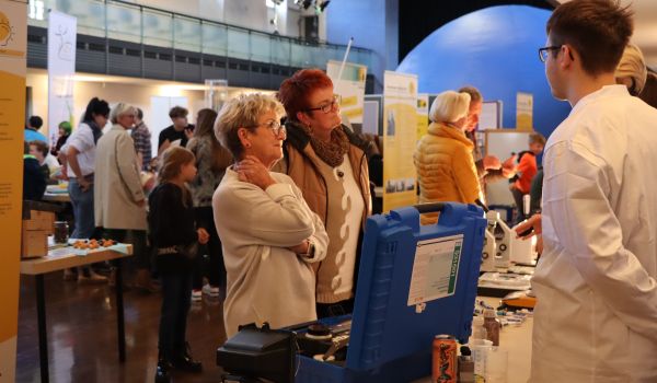 Zwei Jugendliche in weißen Kitteln erklären Experimente für Interessierte.