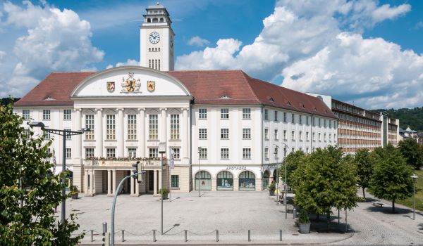EIn weißes Gebäude mit rotem Dach und einem Turm. Es ist das Rathaus der Stadt Sonneberg. Die Sonne scheint.