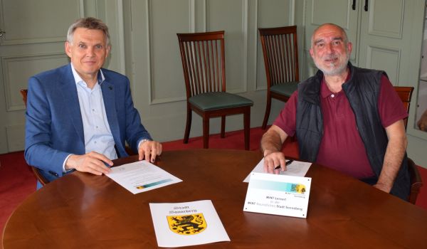 Zwei Männer sitzen an einem Tisch und unterschreiben einen Vertrag.