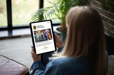 Eine Frau sitzt mit einem Tablet auf der Couch.