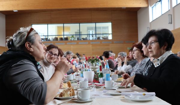 Frauen sitzen an gedeckten Tischen bei Kuchen und Kaffee.