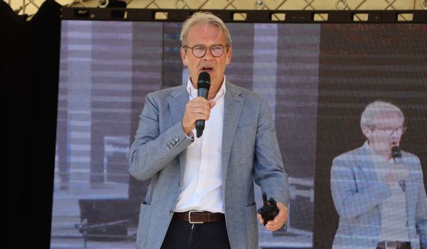 Ein Mann im Anzug steht auf einer Bühne und begrüßt die Gäste.