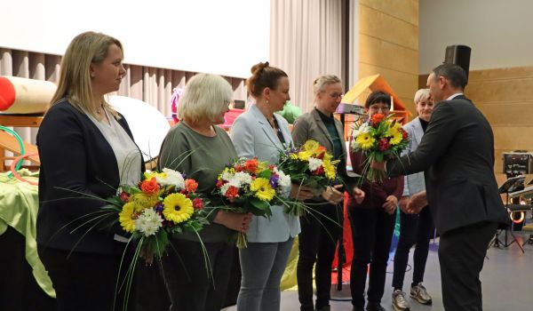 Frauen stehen in einer Reihe. Ein Mann gratuliert sie und überreicht einen Blumenstrauß.