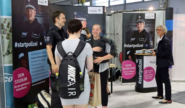 Personen stehen vor Bannern. Auf den Bannern sind junge Polizisten in Uniform abgebildet.