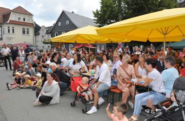 Viele Menschen sitzen auf Bänken unter Sonnenschirmen.