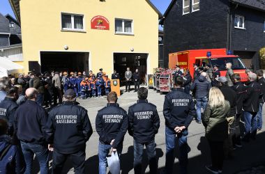 Feuerwehrmitglieder stehen im Kreis vor einem Gebäude. Das Gebäude trägt die Aufschrift: Freiwillige Feuerwehr Spechtsbrunn. Daneben steht ein Feuerwehrfahrzeug.