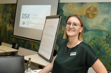 Eine Frau steht vor einer Beamer-Leinwand. Im Hintergrund ist ein Wandgemälde der Wolke 14.