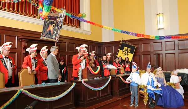 Der Elferrat steht in einer Reihe im Rathaussaal. Rechts daneben sitzen die beiden Prinzenpaare auf einem goldenen Sofa.