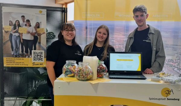 Zwei junge Frauen und ein Mann stehen an einem Infostand. Es sind Auszubildende der Stadt Sonneberg.