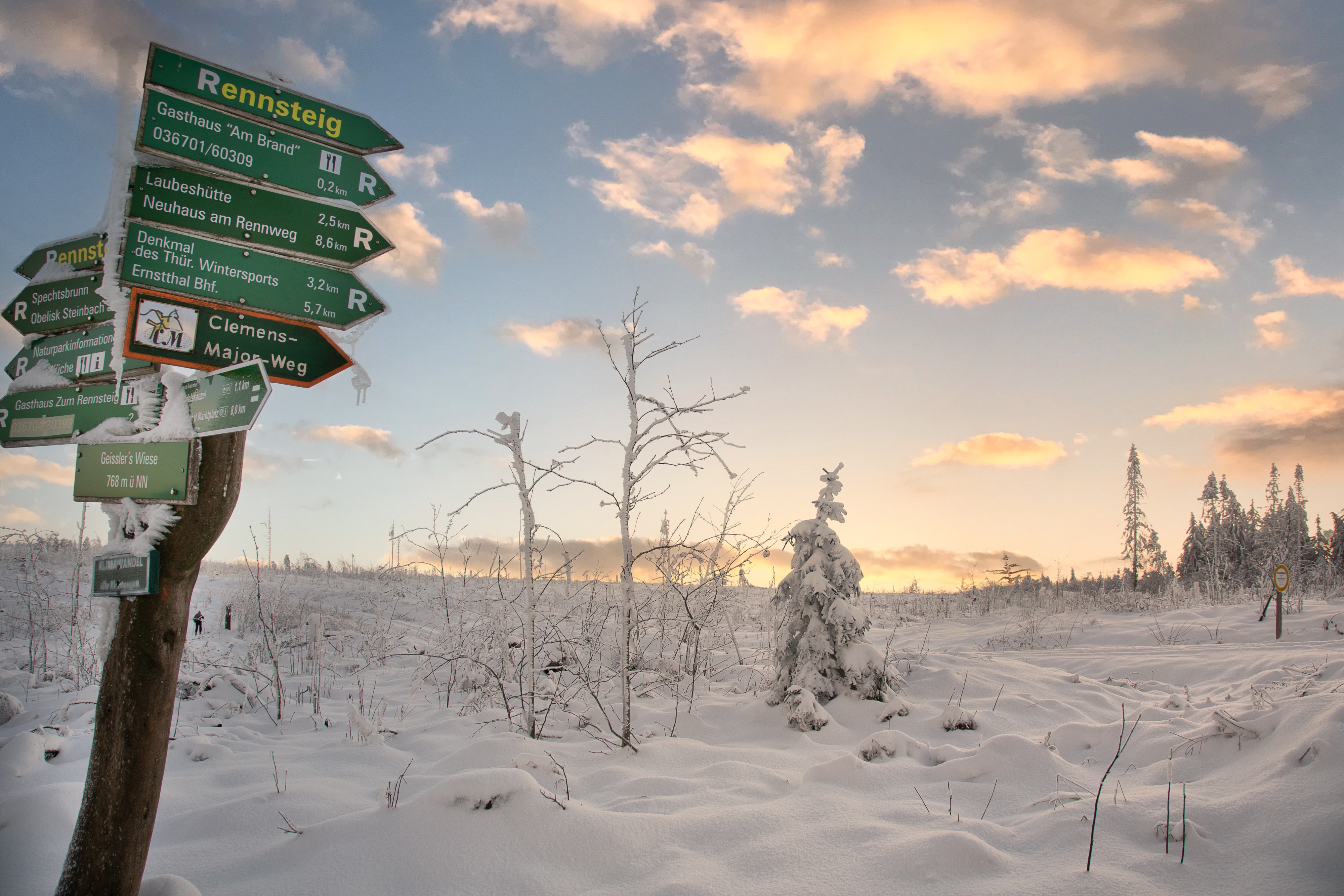 Eine verschneite Winterlandschaft. Links steht ein Wegweiser mit Wanderwegen.