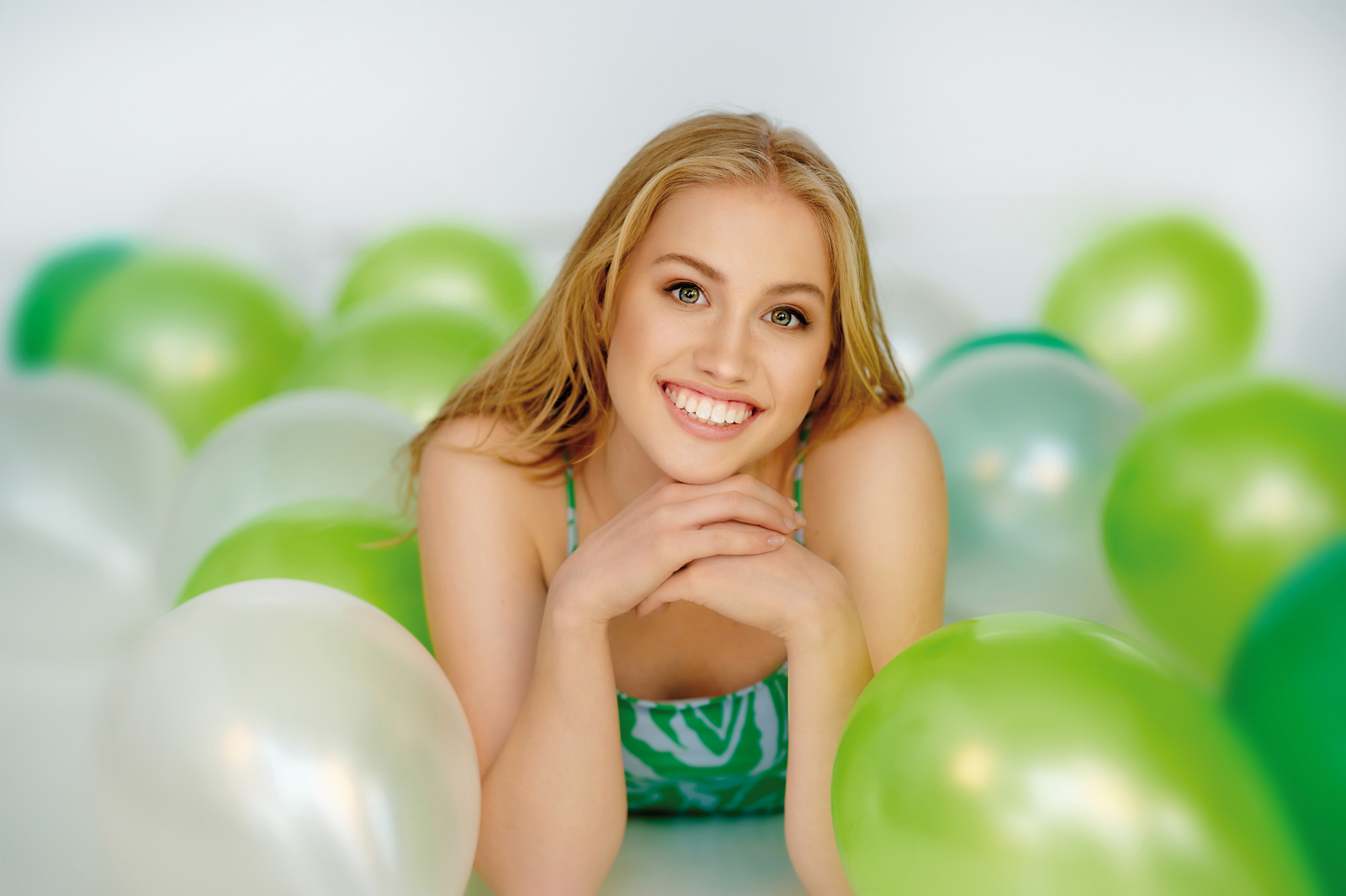 Eine junge Frau liegt auf dem Boden umgeben von weißen und grünen Luftballons.