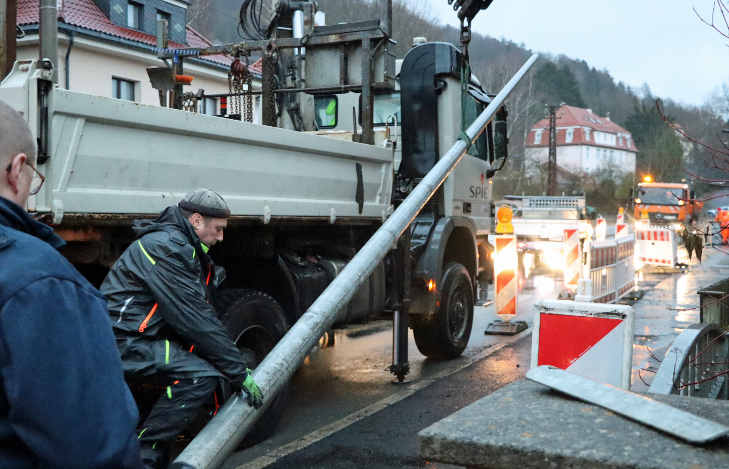 Zwei Bauarbeiter setzen einen Lichtmast auf einem Gehweg.