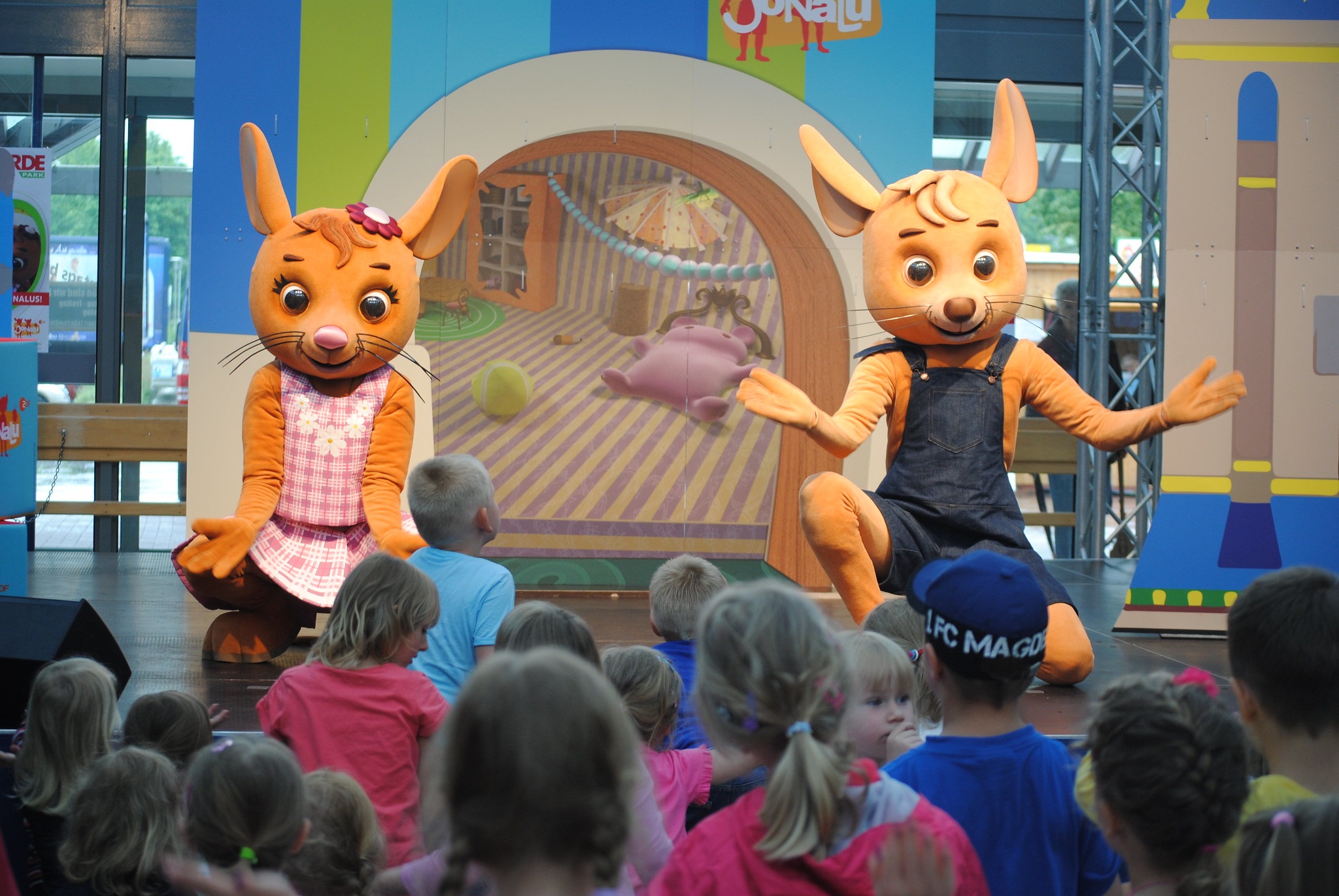 Zwei Mausfiguren stehen auf einer Bühne und davor stehen Kinder.