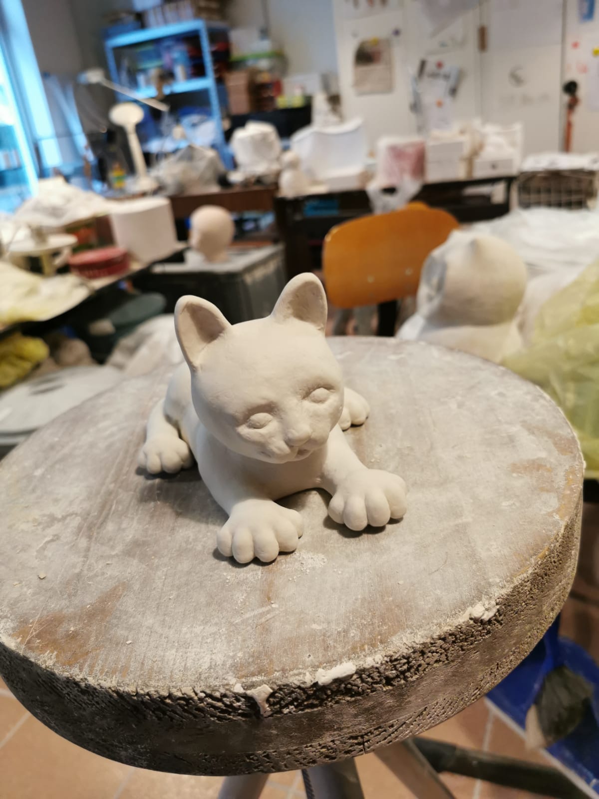 Eine Katze aus Ton modelliert sitzt auf einem Hocker.