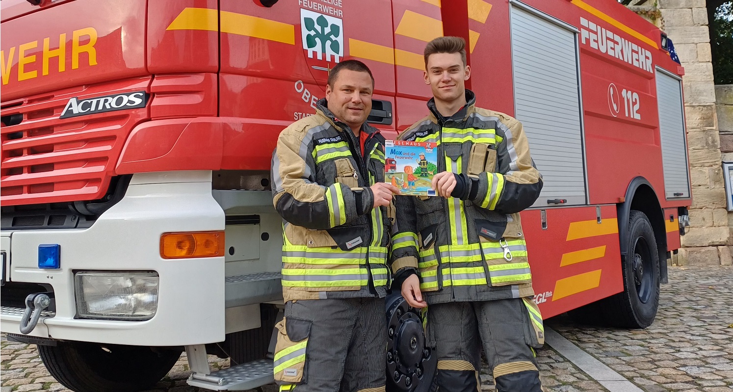 Zwei Feuerwehrkameraden stehen vor einem Feuerwehrauto.