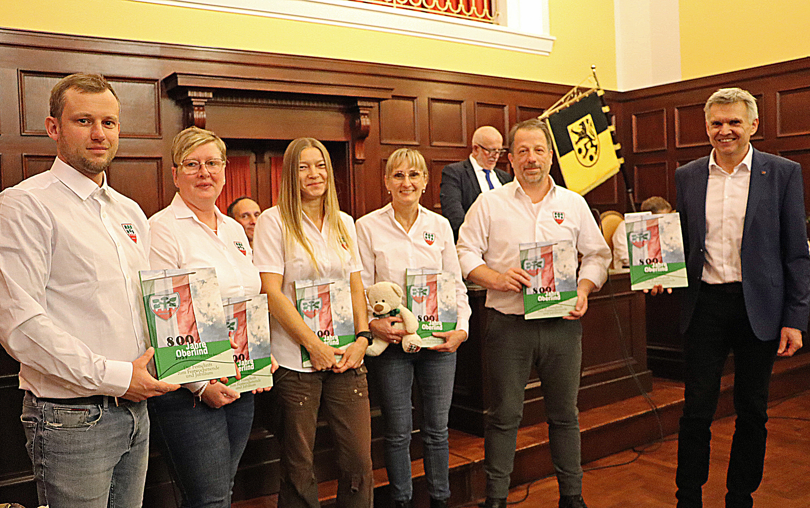 Zwei Männer und drei Frauen in weißen Hemden vom Heimatverein Oberlind werden von einem Mann in Anzug (Bürgermeister) beglückwünscht.