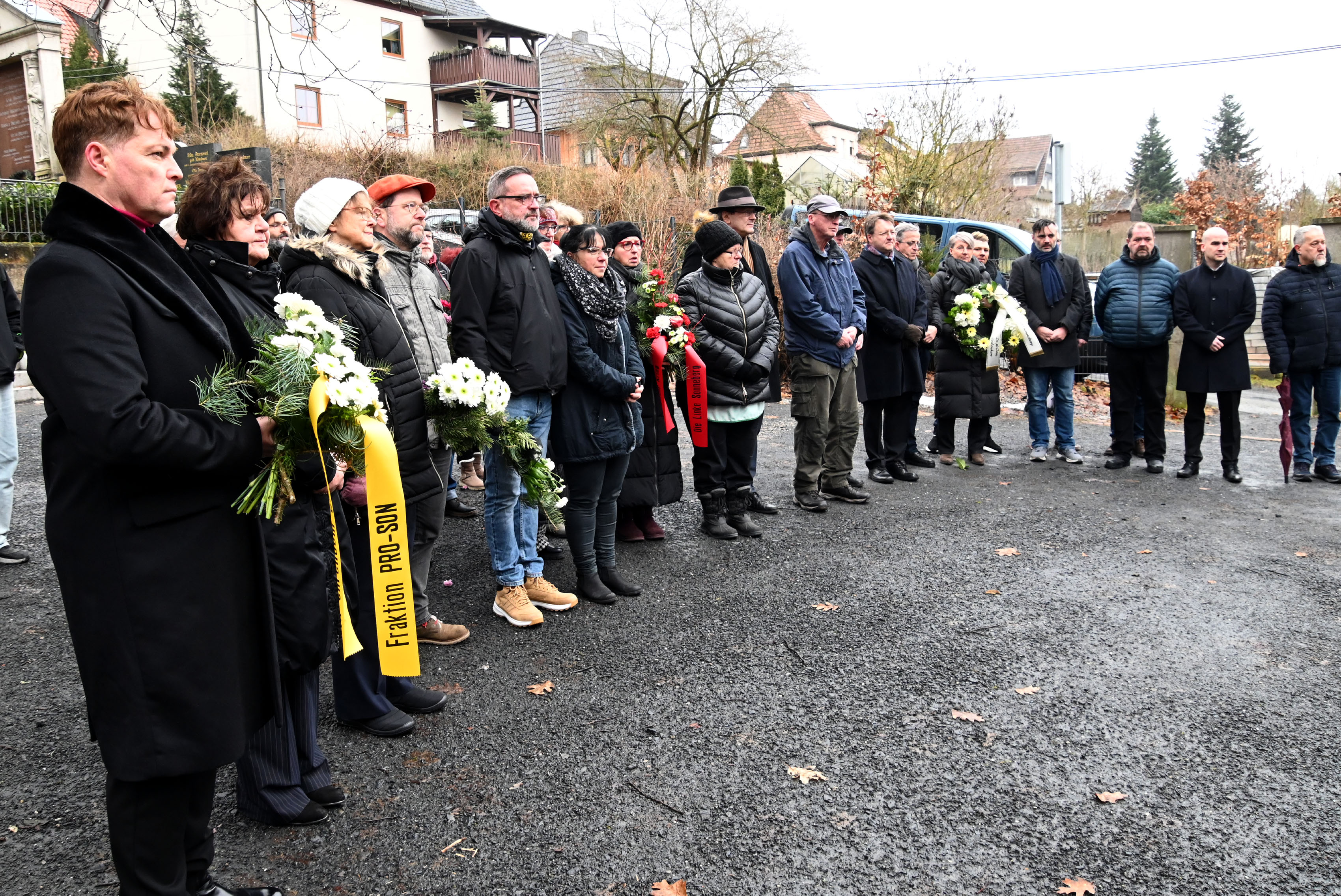 Frauen und Männer stehen im Halbkreis auf einem Friedhof und nehmen an einer Gedenkveranstaltung teil.